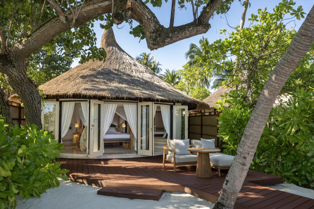 Rundes Bungalow mit Strohdach, Glaswänden und Holzterrasse mit Sesseln im Banyan Tree Vabbinfaru