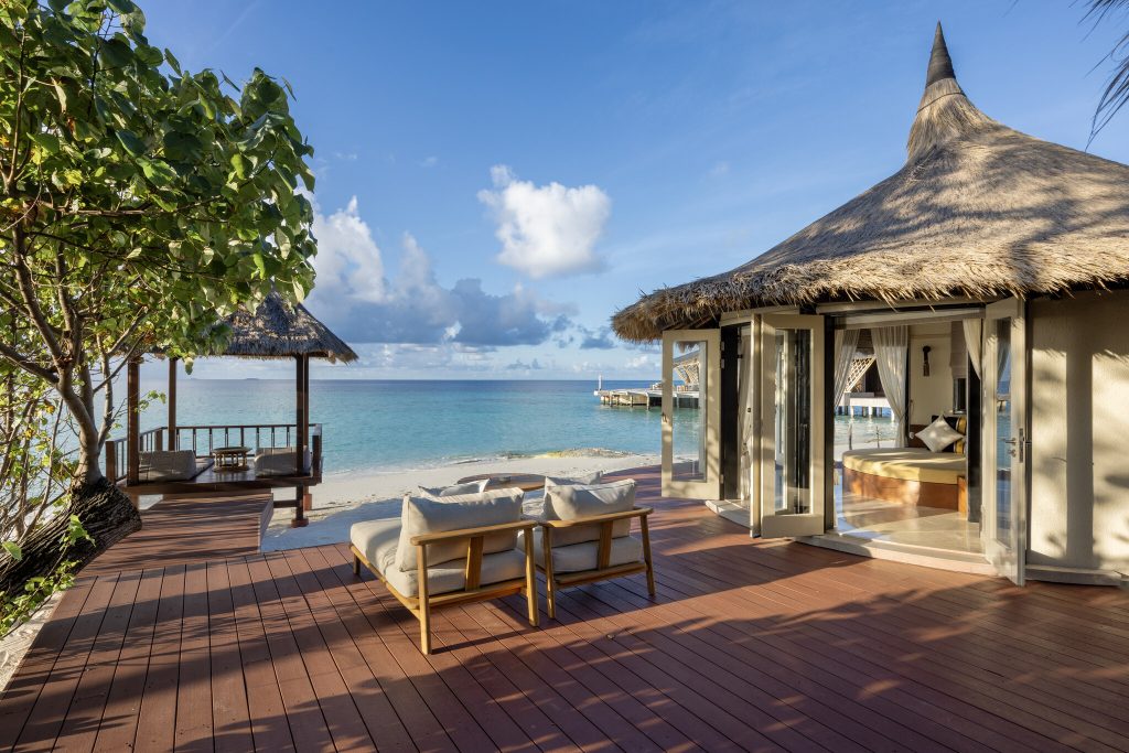 Terrasse mit zwei Liegestühlen und Reetdach-Pavillon vor blauem Meer und Himmel in der Grand Beachfront Pool Villa