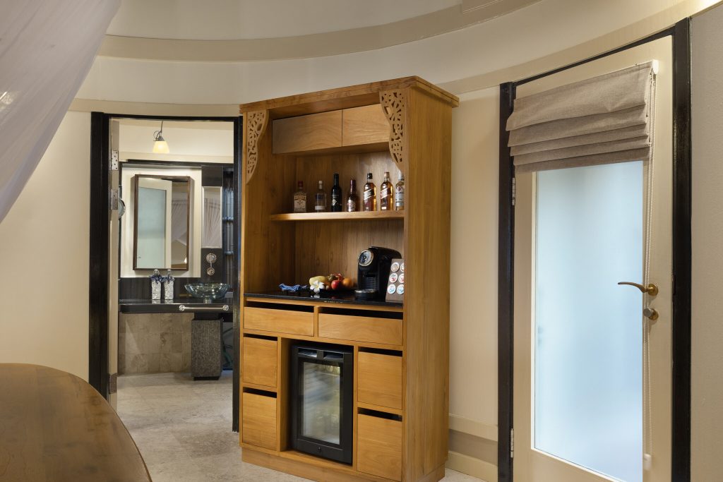 Hotelzimmer mit Holzmöbeln, Getränkeschrank, Kaffeemaschine und offenem Badezimmer mit Glaswaschbecken