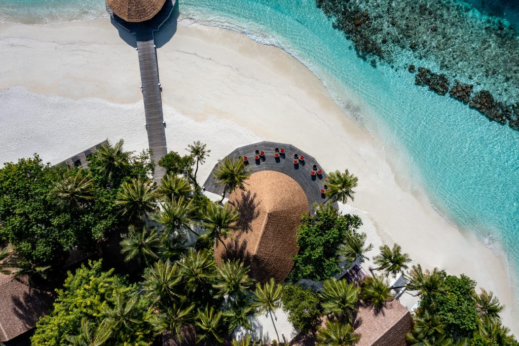 Luftaufnahme der Bar Velaavani mit rundem strohgedecktem Pavillon und Holzsteg am Strand auf den