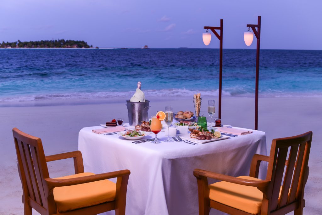 Gedeckter Tisch mit weißen Tischdecken und Holzstühlen am Strand bei Dämmerung im Dhawa Ihuru Restaurant