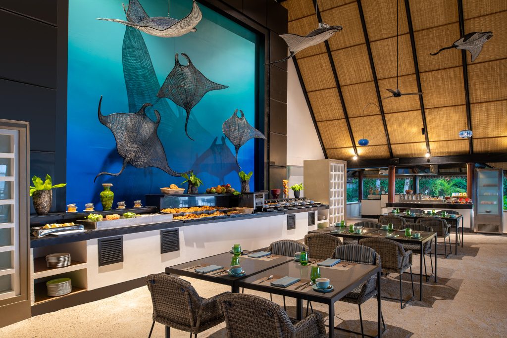 Restaurant Riveli im Dhawa Ihuru mit Buffet, Holzbalkendecke, Rattanstühlen und blauem Manta-Wandbild