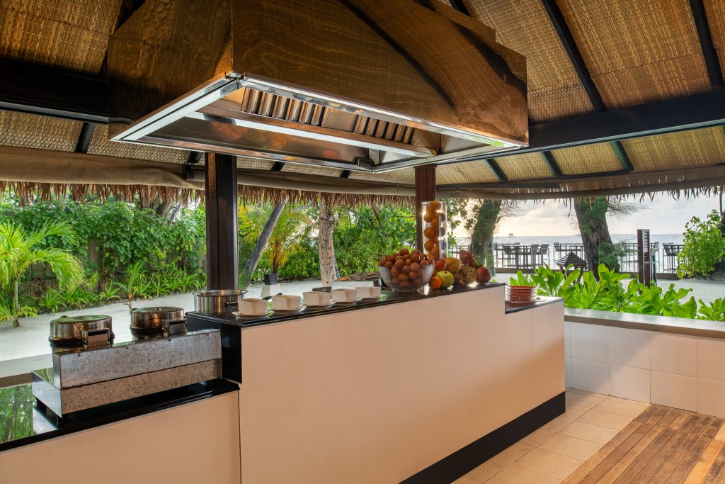 Offene Hotelküche im Restaurant Riveli mit Töpfen, Holz- und Metallmaterialien, tropischer Landschaft und Meer im Hintergrund