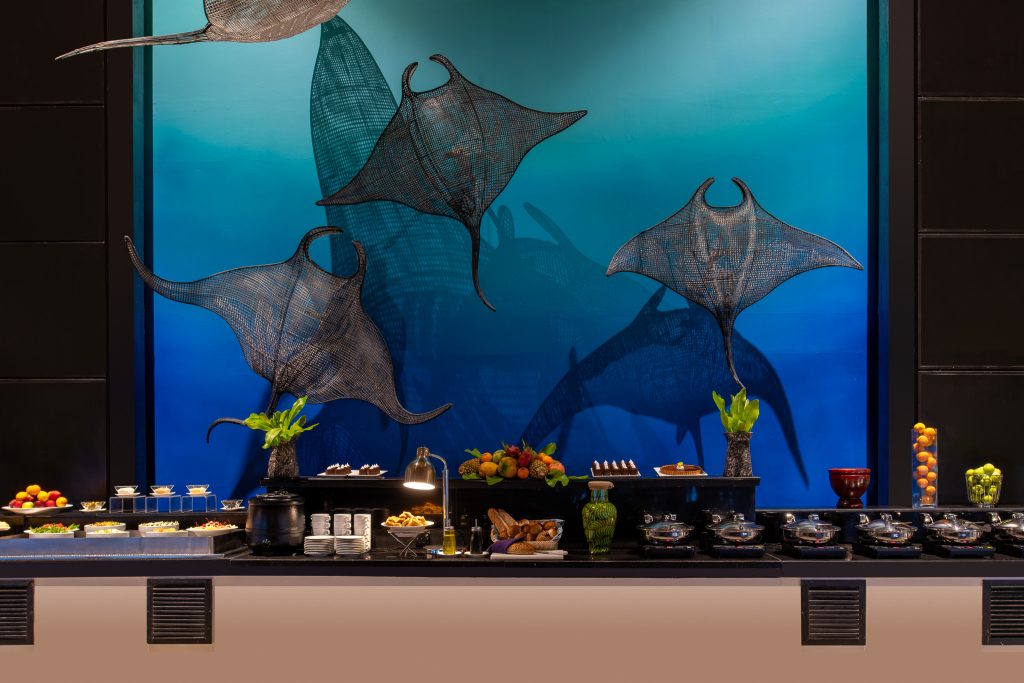 Buffet im Restaurant Riveli mit Draht-Rochen Wanddeko, blauem Farbübergang und vielfältigen Speisen
