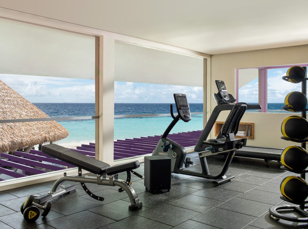 Fitnessraum Dhawa Ihuru mit Liegefahrrad, Hantelbank und großen Fenstern zum Meer auf den
