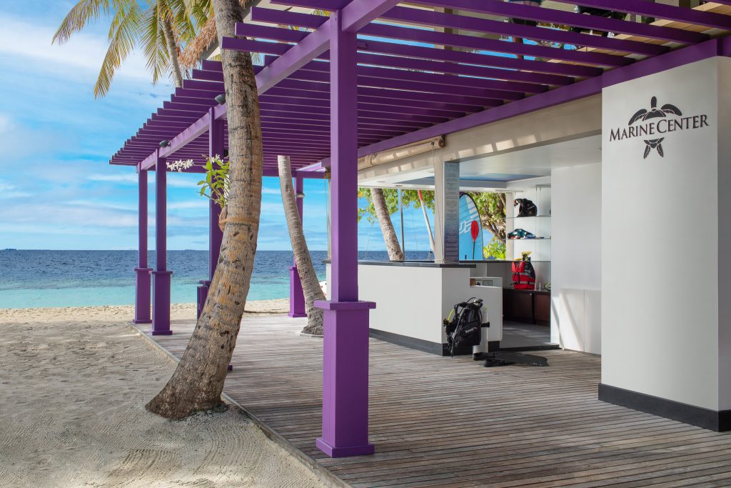 Offener lila Pavillon als Marine-Center mit Holzplanken am weißen Sandstrand und türkisblauem Meer auf den