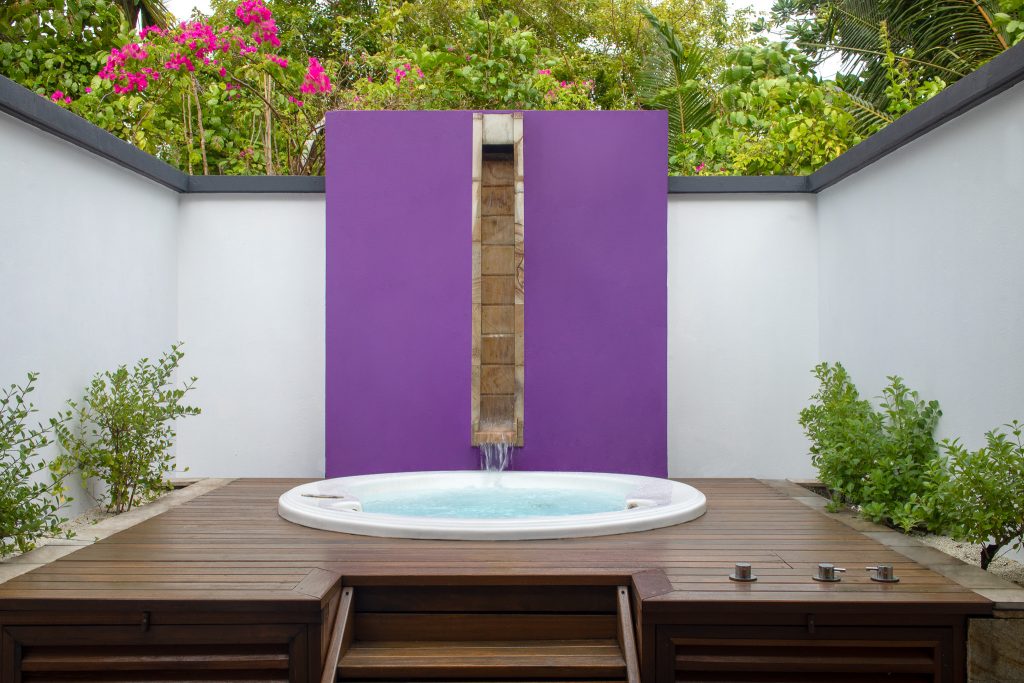 Moderner Außenbereich mit rundem Whirlpool auf Holzterrasse, violette Wand mit Wasserfall.