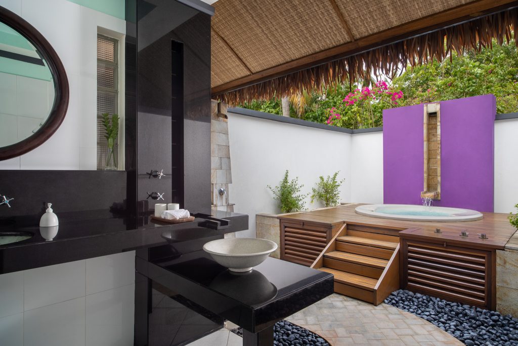 Badezimmer in der Beachfront Jet Pool Villa Dhawa Ihuru mit schwarzem Waschbecken, rundem Spiegel und offenem Bad.