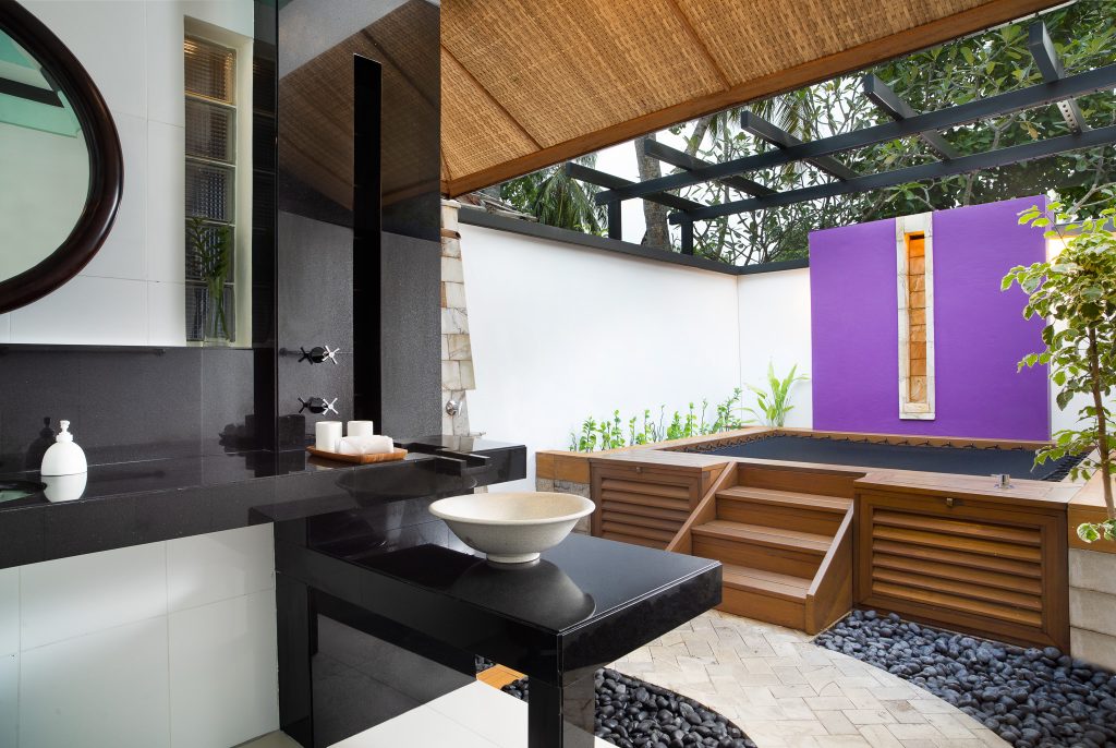 Badezimmer der Beachfront Rainmist Villa im Dhawa Ihuru mit schwarzer Steinplatte, rundem Spiegel und integriertem.