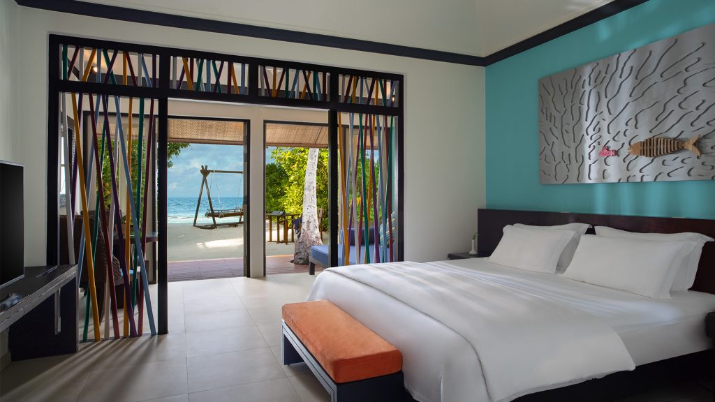 Modernes Hotelzimmer der Dhawa Ihuru Beachfront Sunset Villa mit großem Bett, Metall-Wandbild und Meerblick