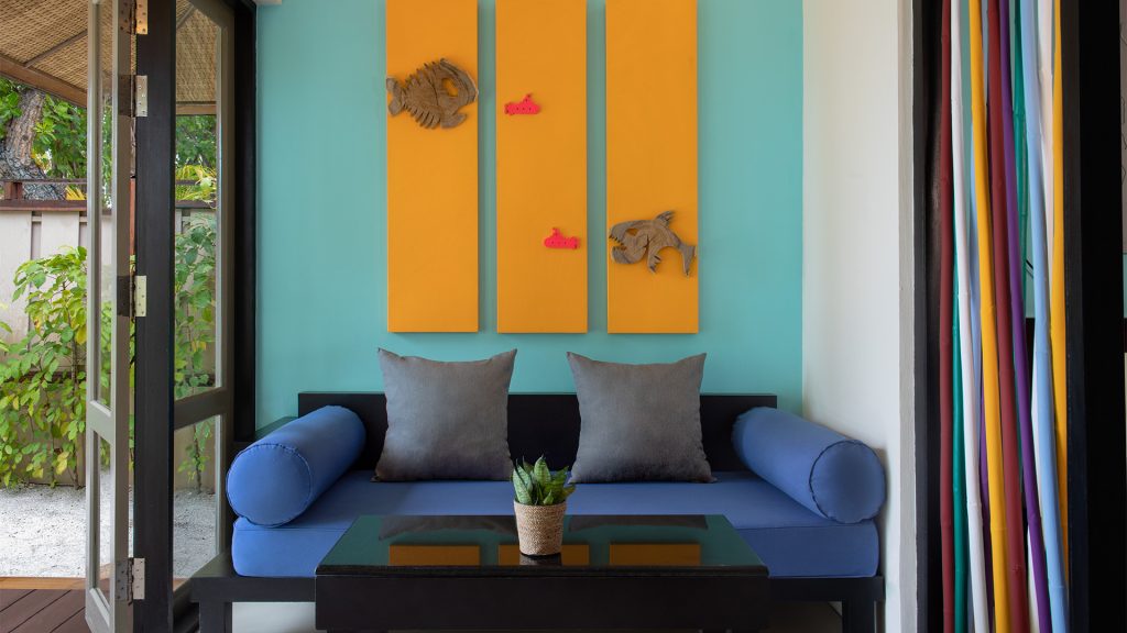 Moderner Innenraum mit blauem Sofa, türkisfarbener Wand, orangen Fisch-Kunstwerken und Blick auf Terrasse mit Grün