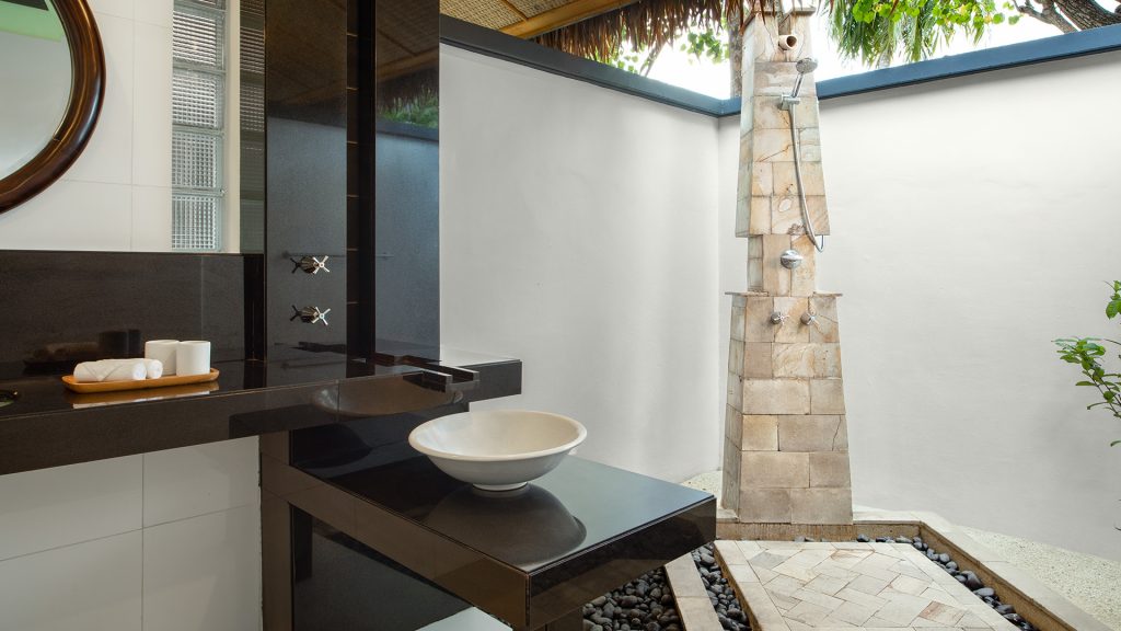 Badezimmer mit offenem Duschbereich, schwarzem Steinwaschbecken und beiger Natursteindusche in der Beachfront Sunset Villa