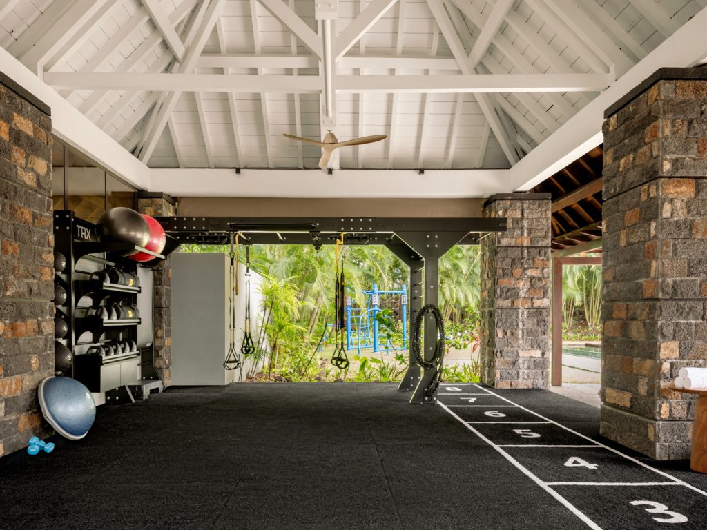 Offener Fitnessraum mit Holzkonstruktion, weißen Dach, grauen Steinpfeilern, TRX-Bändern