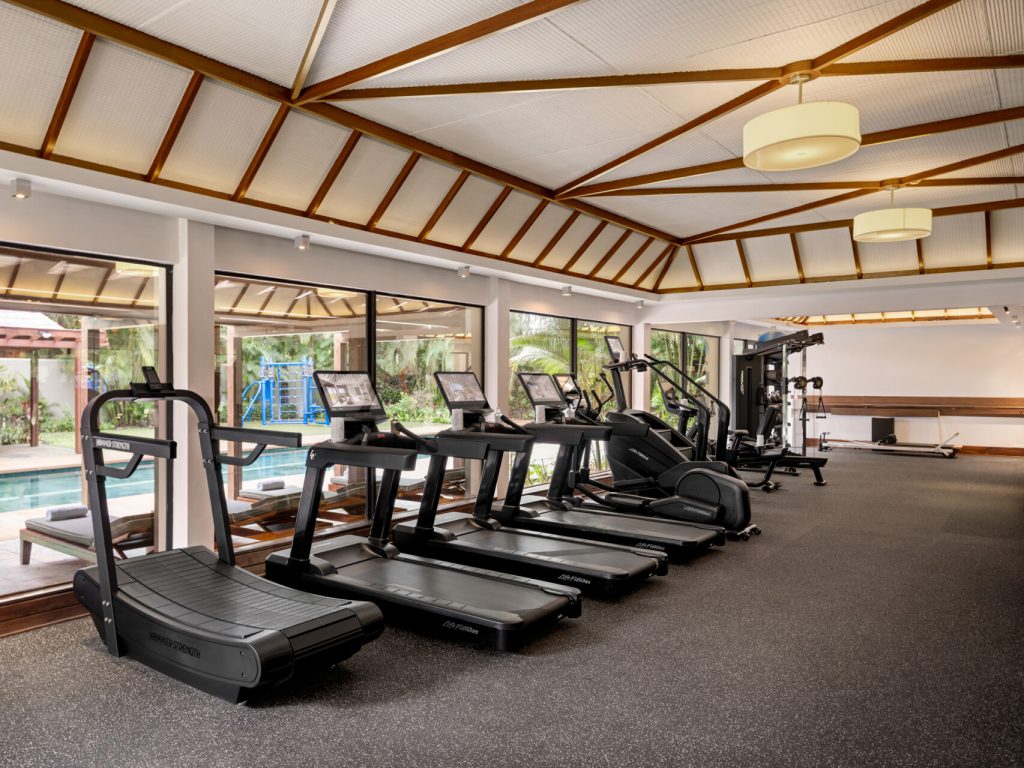 Modernes Fitnessstudio mit Laufbändern, Holzdecke und großen Fenstern mit Blick auf Pool