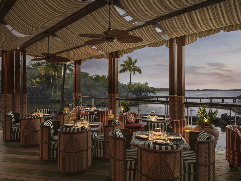Outdoor-Restaurantterrasse mit Korbmöbeln, Holztischen, Stoffdach und Blick auf tropische Landschaft und Meer