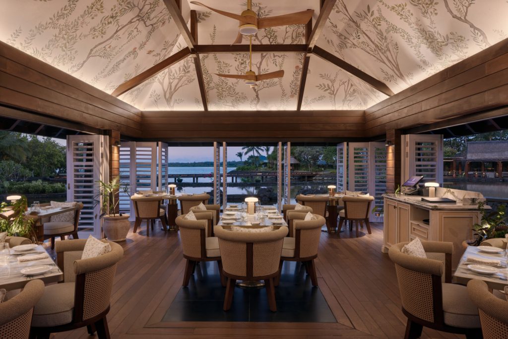 Restaurant Allgemein mit Holzbalkendecke, gepolsterten Stühlen, weißen Tischsets und Blick auf Wasserlandschaft