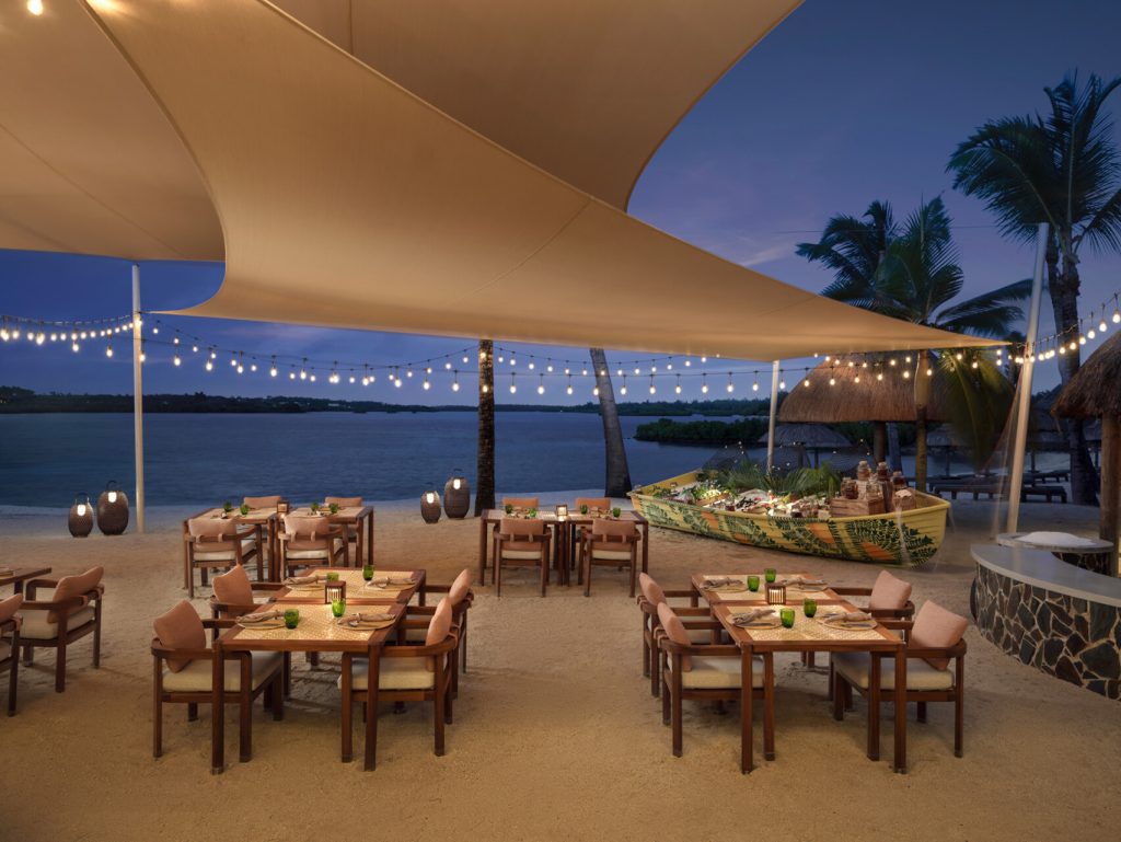Strandrestaurant Four Seasons Resort Mauritius At Anahita mit Holztischen, rosafarbenen Polstern und Lichterketten.