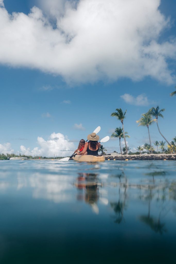 Paar paddelt in Kajak auf ruhigem tropischem Wasser mit Palmen und blauem Himmel im Hintergrund