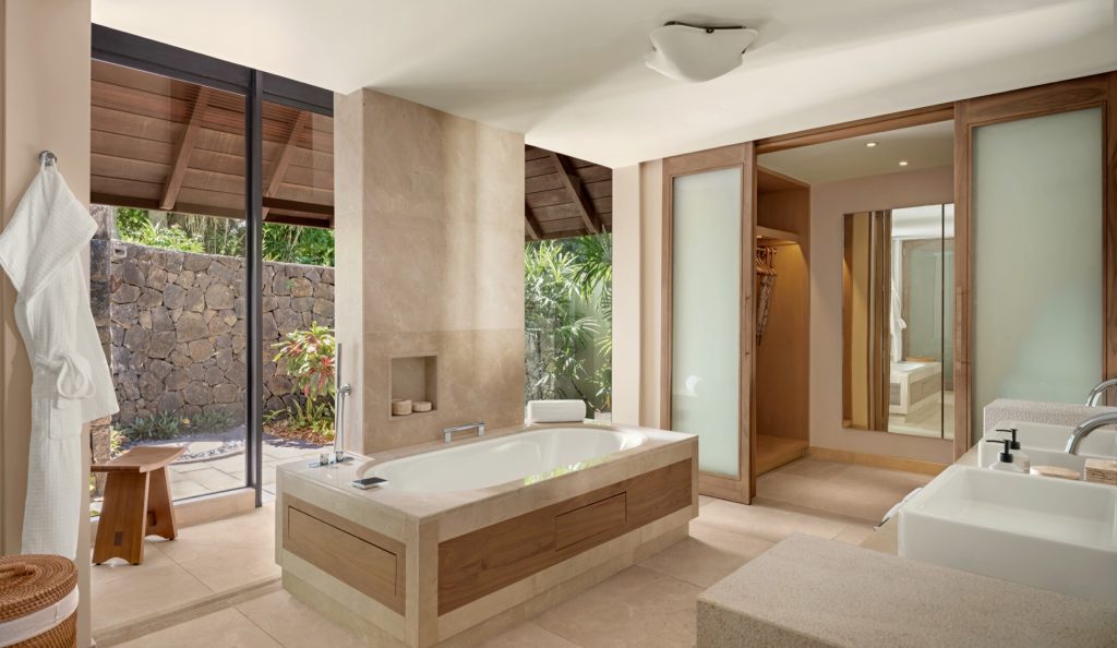 Badezimmer mit freistehender Marmorbadewanne, Glaswand zum bepflanzten Außenbereich und Holz-Stein-Elementen
