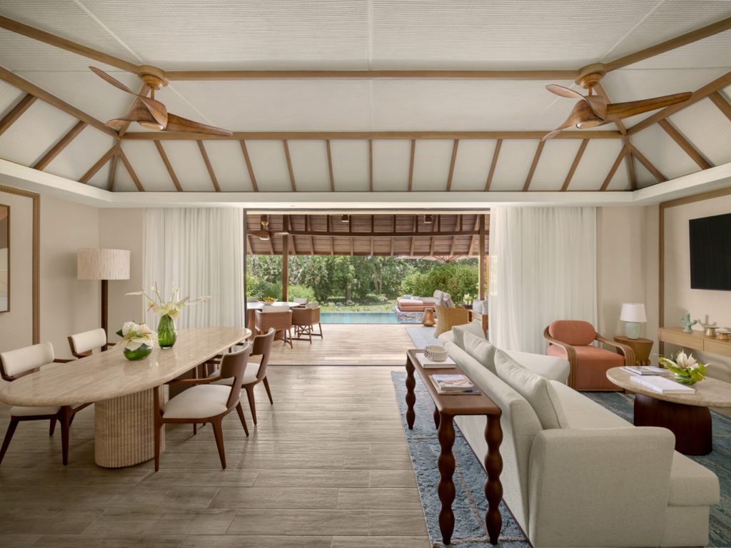 Hotelwohnraum mit Holz-Esstisch, Sofa und offenem Zugang zum Außenbereich mit Pool im Four Seasons Resort Mauritius At.
