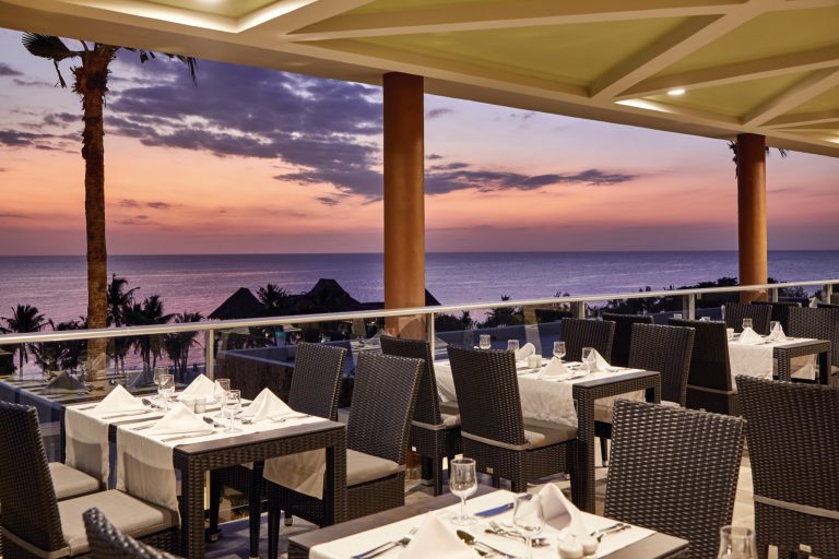 Hotel Riu Jambo Restaurant-Terrasse mit Rattanmöbeln, weißen Tischdecken und Meerblick bei Sonnenuntergang