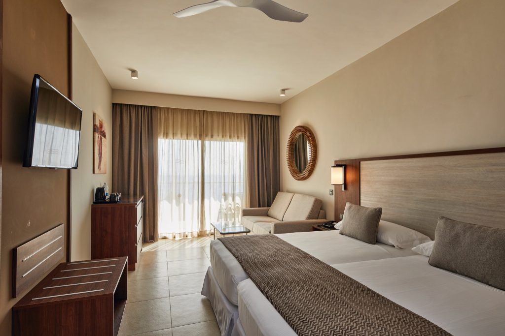 Doppelzimmer im Hotel Riu Jambo mit großem Bett, Zweisitzer-Sofa, Holzschrank und bodentiefen Fenstern