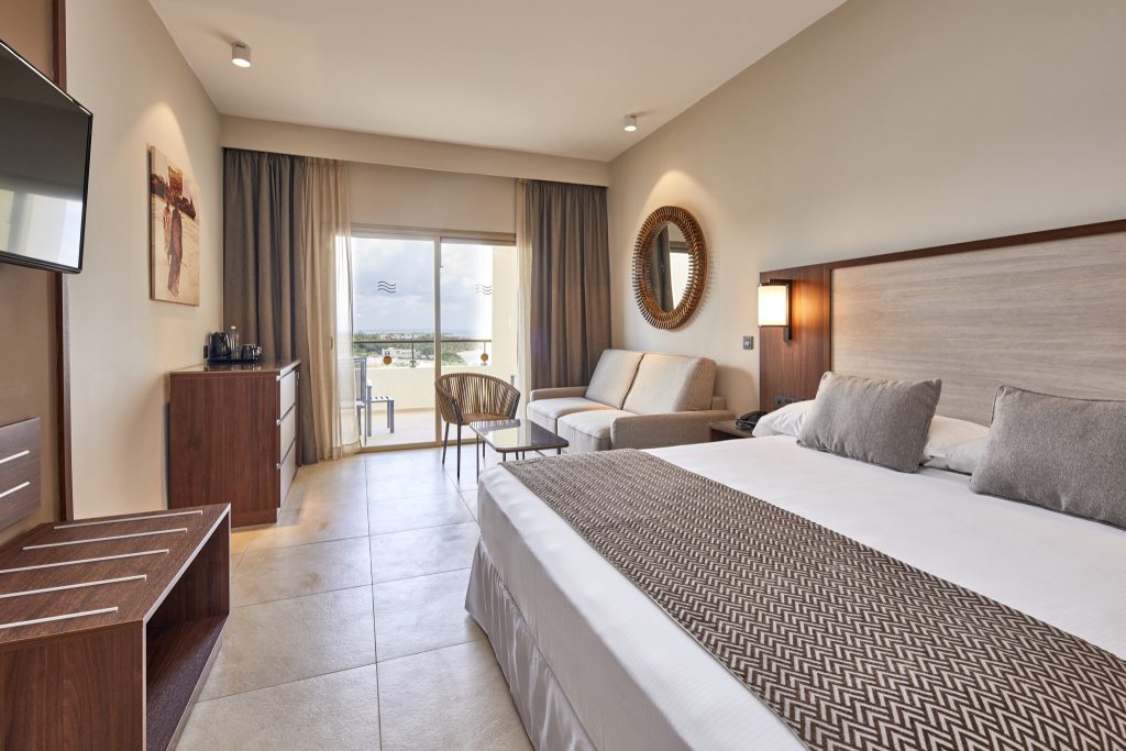 Modernes Hotelzimmer Hotel Riu Jambo Family mit großem Bett, Couch, Glastisch und Balkon in Sansibar
