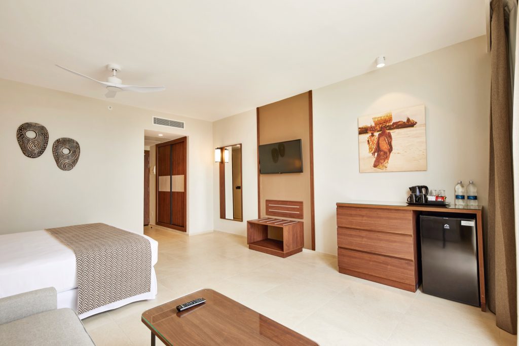 Modernes Hotelzimmer Superior im Hotel Riu Jambo mit Doppelbett, weißer Bettwäsche, Holzmöbeln und Kunstwerk