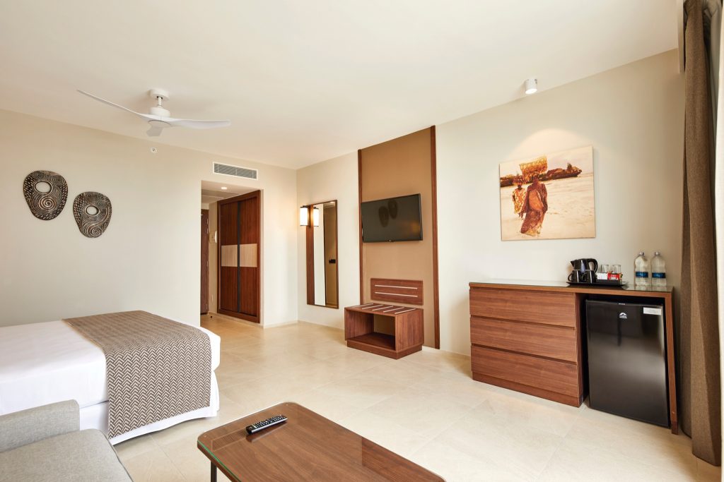 Modernes Hotelzimmer Superior Sea View mit großem Bett, weißer Bettwäsche, brauner Überdecke und Holzmöbeln im Hotel Riu.