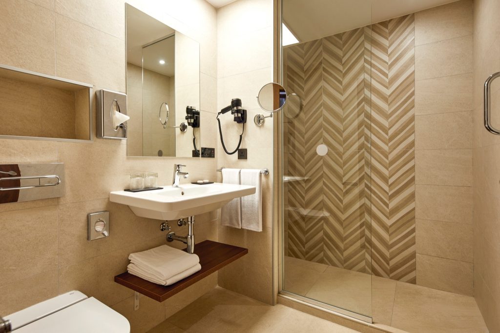 Modernes Badezimmer im Hotel Riu Jambo Superior Sea View mit Waschbecken, Spiegel, Handtuch und Dusche mit Zickzackfliesen