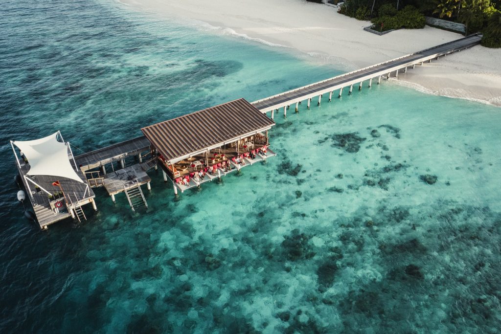 Bar Dive Bar Terrasse auf Stelzen über türkisfarbenem Wasser mit Holzsteg und roten Stühlen auf den