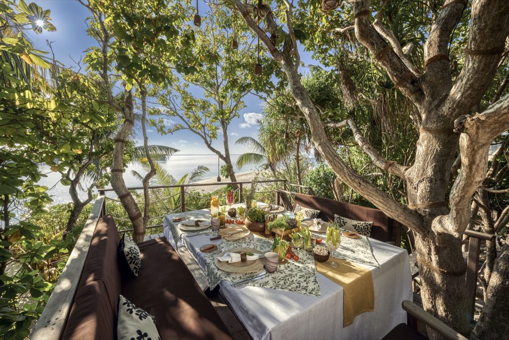 Outdoor-Terrasse mit gedecktem Tisch, gepolsterten Bänken und Blick auf den Ozean im Restaurant Chefs Garden Treehouse