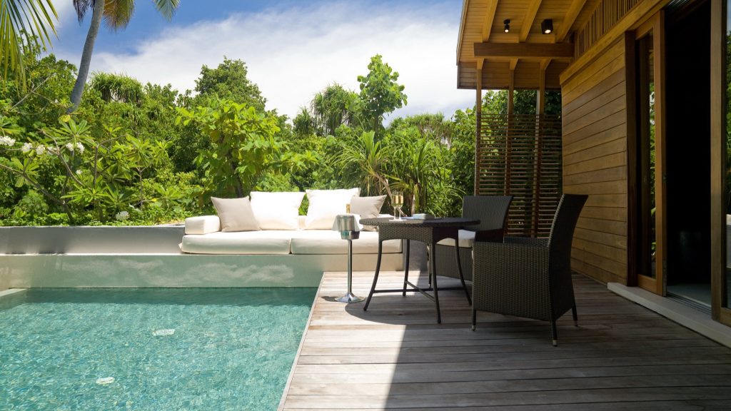 Moderne Terrasse mit Holzdeck, Sofa mit beigen Kissen, dunklem Tisch mit Stühlen und kleinem Pool auf den