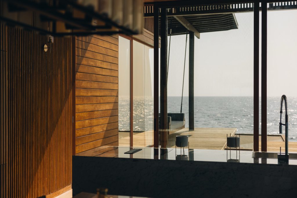 Moderner Innenraum der Kiaali Residence im Park Hyatt Maldives Hadahaa mit Holzverkleidungen und Meerblick durch große.