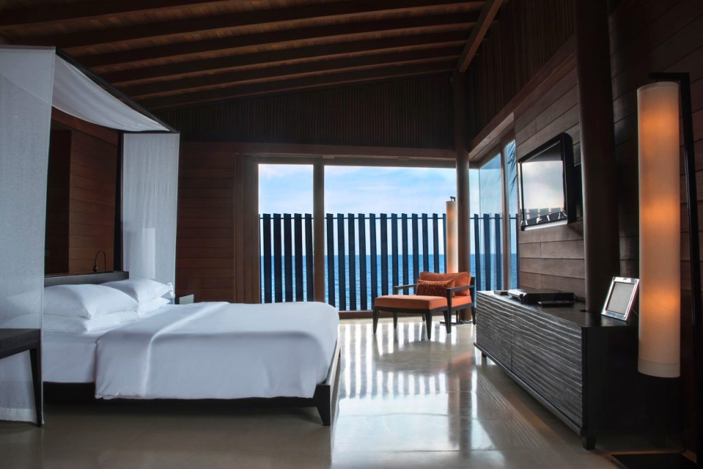 Modernes Hotelzimmer mit Baldachinbett, Holzdecke, Glasfront und Meerblick in Overwater Sunset Villa