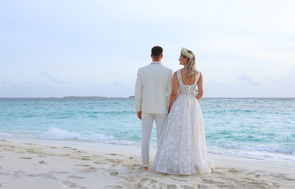 Paar am hellen Sandstrand mit bläulichem Meer und leicht bewölktem Himmel im Reethi Faru Resort Malediven