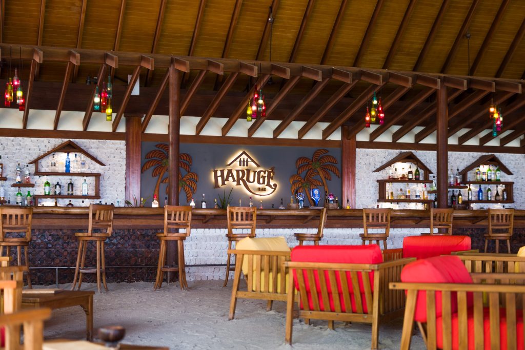 Bar Haruge im Reethi Faru Resort mit Holzdach, Holzstühlen, bunten Kissen und Glaslampen auf den