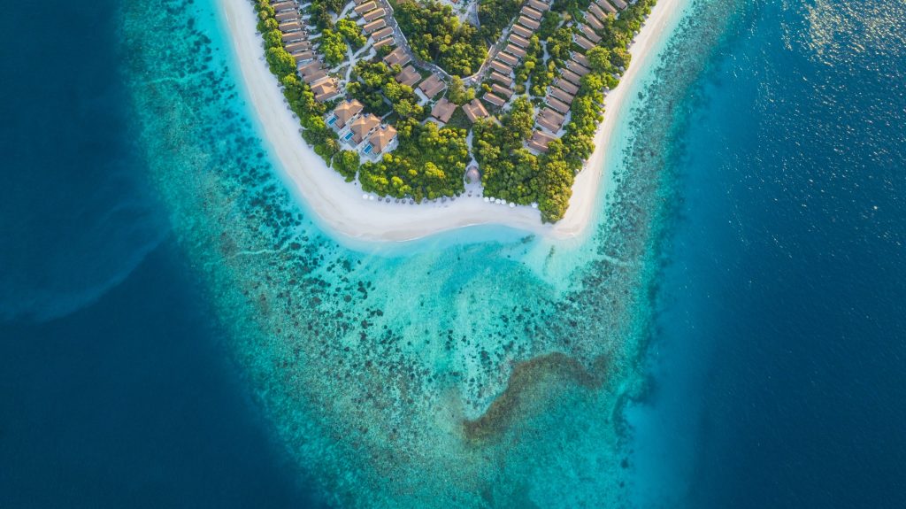 Luftaufnahme des Reethi Faru Resorts mit Reihen roter Bungalows, weißem Sandstrand und türkisblauem Meer auf den