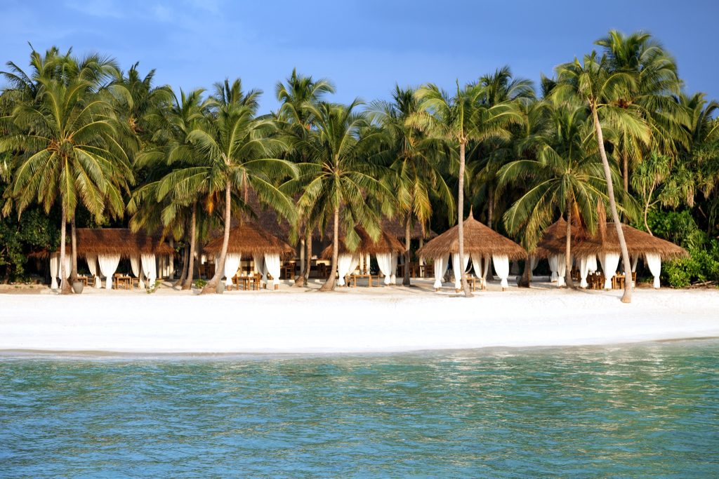 Reethi Grill Restaurant mit Holzpavillons, weißen Vorhängen und Palmen am Strand