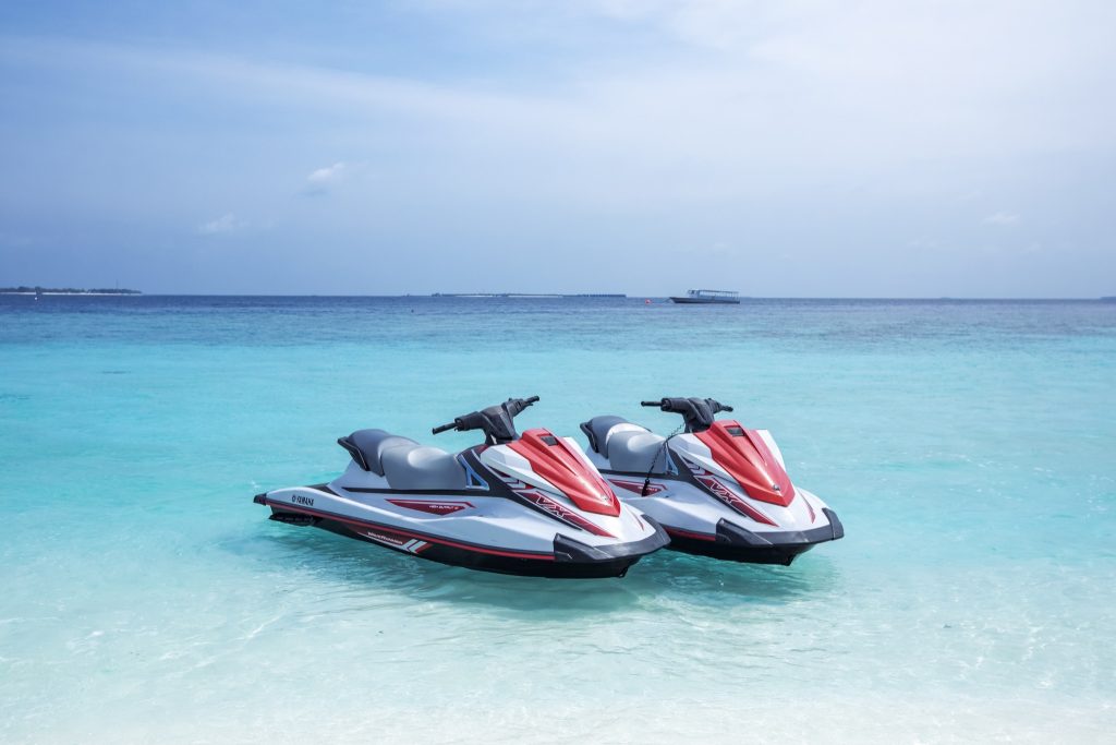 Zwei weiße und rote Jetskis auf klarem türkisfarbenem Wasser mit Ozean und Boot im Hintergrund