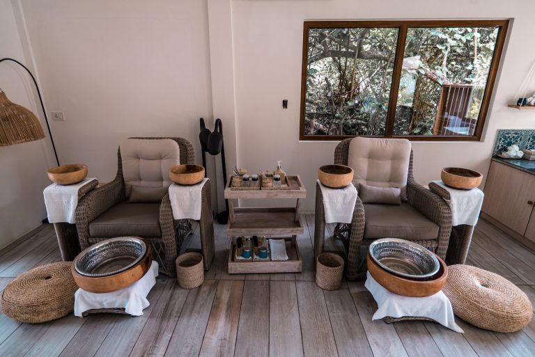 Spa-Bereich im Reethi Faru Resort mit zwei beigen Rattansesseln, Holzbeistelltisch und Fußbädern auf weißen Handtüchern