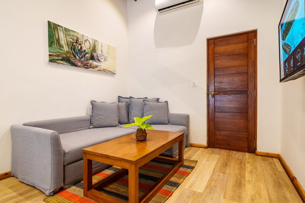Zimmer der 2BR Garden Suite im Reethi Faru Resort mit grauem Sofa, Holztisch, Pflanze und Gemälde an der Wand