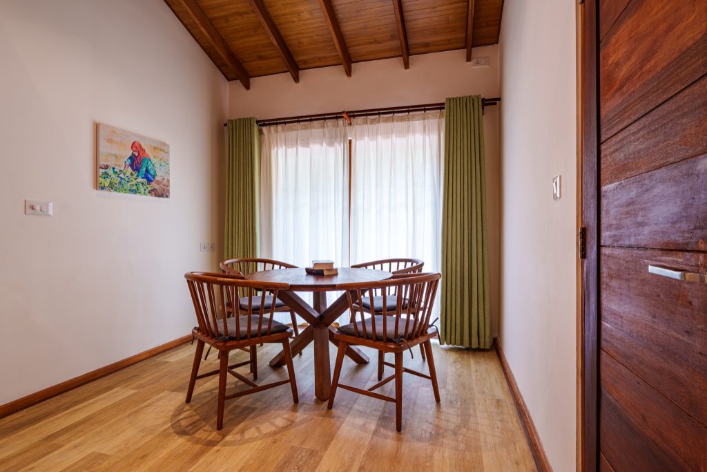 Essbereich mit rundem Holztisch, vier Holzstühlen, hellen Wänden und grünen Vorhängen im 2BR Garden Suite Zimmer