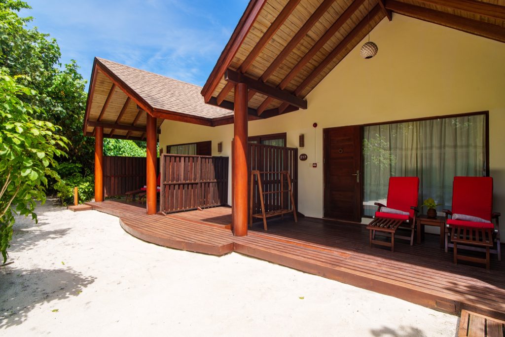 Terrasse der 2BR Garden Suite im Reethi Faru Resort mit Holzdielen, roten Liegestühlen und grünem Pflanzenrahmen