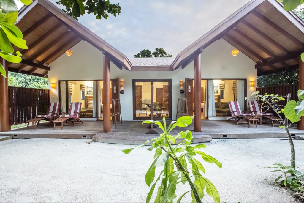 Vorderansicht zweier 2BR Garden Suites im Reethi Faru Resort mit Holzliegen auf Holzdeck und sandigem Untergrund