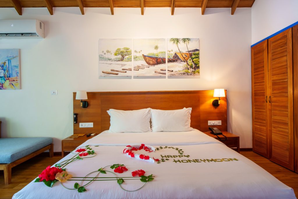 Zimmer der Deluxe Beach Pool Villa im Reethi Faru Resort mit großem Bett, Wandmalerei und Holzkleiderschrank
