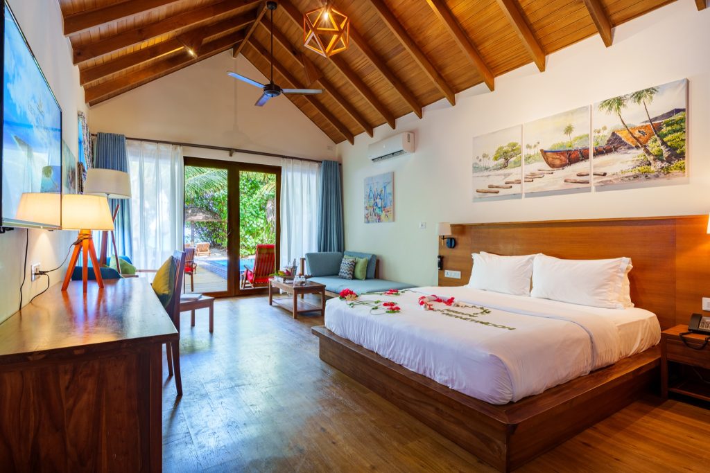 Geräumiges Zimmer der Deluxe Beach Pool Villa mit Holzdach, großem Bett, Schreibtisch und Blick auf Veranda mit Pool auf den.