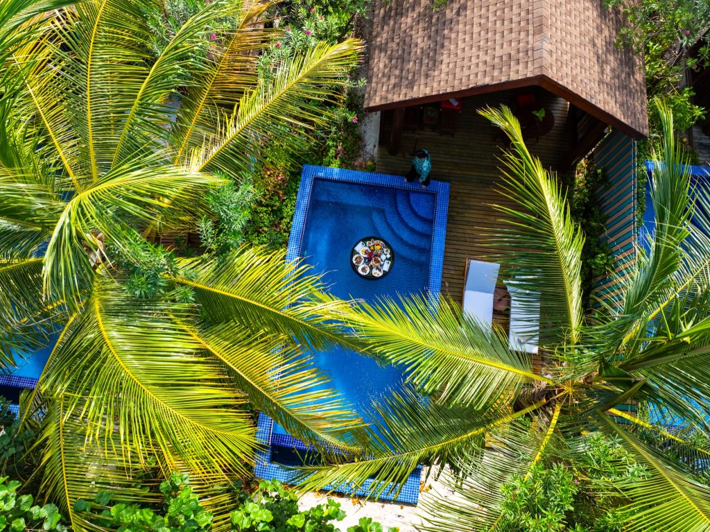 Blick von oben auf Reethi Faru Resort Deluxe Beach Pool Villa mit rechteckigem Pool und schwimmendem Frühstücksbrett