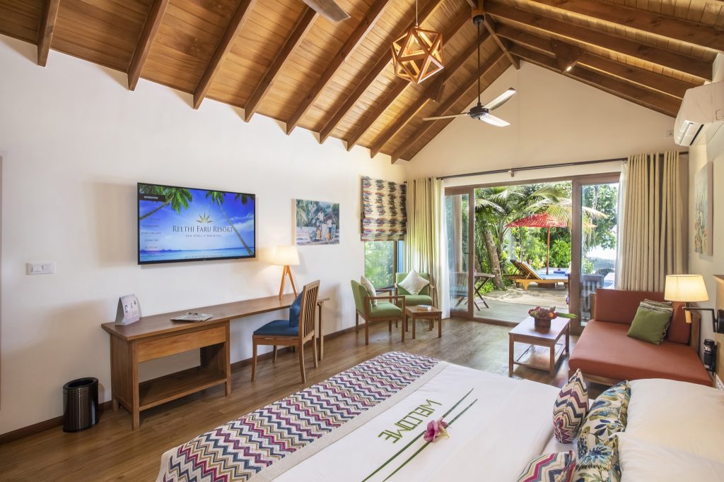 Zimmer der Deluxe Beach Pool Villa im Reethi Faru Resort mit Holzdach, Flachbildfernseher und großer Glasfront