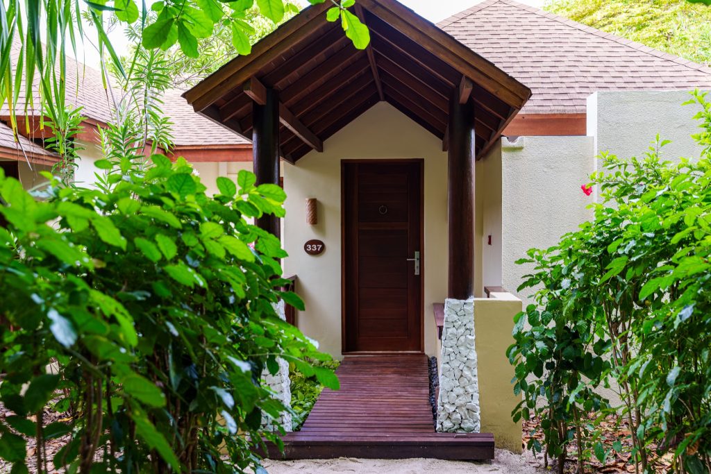 Eingangsbereich der Deluxe Beach Villa im Reethi Faru Resort mit Holzweg und grünem Laub